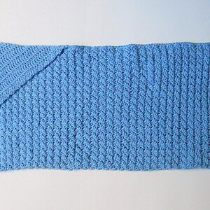 May include: A light blue crocheted baby blanket with a folded corner.
