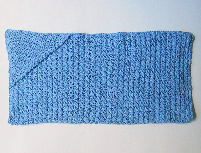 May include: A light blue crocheted baby blanket with a folded corner.