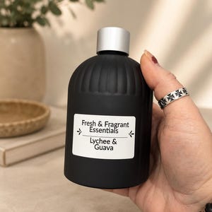 May include: A matte black bottle with a silver cap and a white rectangular label. The label features the text Fresh & Fragrant Essentials and Lychee & Guava with decorative arrows. The bottle has a ribbed texture along the upper portion.