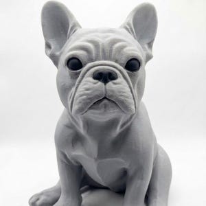 Könnte beinhalten: Eine matte hellgraue Figur einer Französischen Bulldogge in aufrechter Sitzposition. Die Skulptur zeigt detaillierte Gesichtsfalten, große spitze Ohren und glatte schwarze Augen, die die charakteristischen körperlichen Merkmale der Hunderasse einfangen.