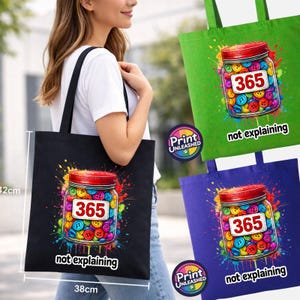 May include: A black, green, and purple tote bag set featuring a graphic of a glass jar filled with colourful buttons. The jar label reads 365, and the text below reads not explaining. The bags measure 38cm by 42cm as indicated by the visible ruler.