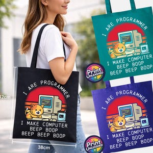 May include: A black, teal, or purple tote bag featuring a graphic of a cat sitting at a computer with the text I ARE PROGRAMMER I MAKE COMPUTER BEEP BOOP BEEP BEEP BOOP. The bag measures 38 cm wide by 42 cm high as indicated by the visible ruler.