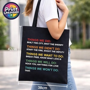 May include: A black tote bag measuring 42cm by 38cm featuring colourful text: THINGS WE DID: BUILT THIS CITY, SHOT THE SHERIFF; THINGS WE DIDN'T DO: START THE FIRE, SHOOT THE DEPUTY; THINGS WE WANT TO DO: BREAK FREE, KNOW WHAT LOVE IS; THINGS WE WILL DO: ROCK YOU, ANYTHING FOR LOVE; THINGS WE WON'T DO: THAT.