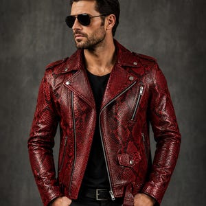 May include: A red and black snakeskin-patterned leather motorcycle jacket featuring a notched lapel, silver-tone metal zippers on the front and sleeves, a small flap pocket, and an adjustable belt at the waist with a silver-tone metal buckle.