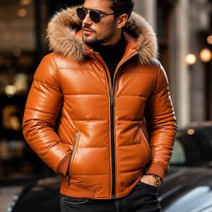 Puede incluir: Una chaqueta acolchada de cuero naranja con capucha y borde de piel sintética marrón, cierre de cremallera frontal negro, puños acanalados y dos bolsillos laterales con cremallera, combinada con un jersey de cuello alto negro y vaqueros oscuros.