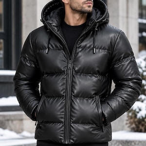 Könnte beinhalten: Eine schwarze Daunenjacke mit glatter, lederartiger Oberfläche, ausgestattet mit einem durchgehenden Frontreißverschluss, einer Kapuze mit verstellbaren Kordelzügen und zwei Seitentaschen. Die Jacke hat ein gestepptes, horizontal unterteiltes Design.