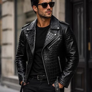 May include: A black motorcycle jacket with a textured crocodile-skin pattern, featuring a wide notched collar, silver-tone metal zips, snap button lapels, and an adjustable waist belt with a buckle, worn over a plain black t-shirt and black trousers.