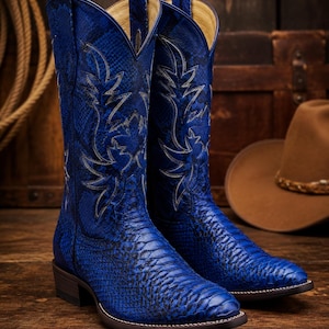 Peut inclure: Une paire de bottes de cow-boy bleu vif présentant un motif texturé en peau de serpent sur tout le cuir. Les bottes ont un bout pointu, un talon bottier et des détails de surpiqûres blanches formant un motif décoratif sur la tige haute.
