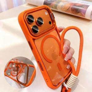 May include: A bright orange smartphone case with a clear back panel, a circular magnetic ring, and a metallic orange camera lens protector featuring the word BRACKET. The case includes an attached orange woven lanyard with a white ribbed connector.