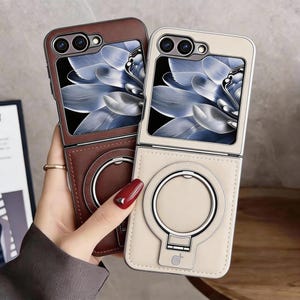 May include: Two foldable phone cases, one dark brown and one beige, featuring a leather-like texture. Each case has a rectangular camera cutout at the top, a screen display area with a blue floral graphic, and a circular metal ring stand on the back.