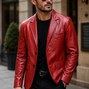 Könnte beinhalten: Ein leuchtend roter Lederblazer mit steigendem Revers, zwei schwarzen Knöpfen auf der Vorderseite und zwei unteren Pattentaschen. Die Jacke wird über einem schlichten schwarzen T-Shirt und einer schwarzen Hose mit schwarzem Ledergürtel getragen. Das Logo PlanioPelle ist sichtbar.