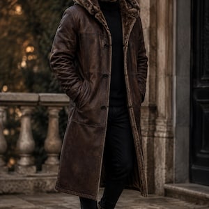 May include: A long, dark brown distressed leather coat featuring a hood lined with thick, textured faux fur. The coat has a button-front closure, long sleeves, and a straight hemline that reaches below the knees, worn over a black turtleneck.