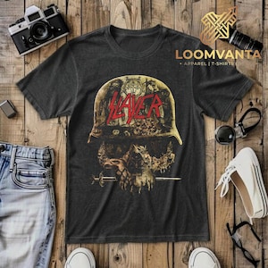 May include: A charcoal grey short-sleeve t-shirt featuring a graphic print of a military helmet resting on a skull. The word SLAYER is printed in bold red letters across the helmet. The design includes intricate, dark, and weathered artistic details.