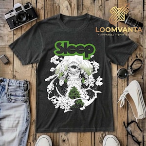 Könnte beinhalten: Ein anthrazitfarbenes Kurzarm-T-Shirt mit einem Grafikdruck eines Astronauten, der von weißen Rauchwolken und einer grünen Pflanze umgeben ist. Das Wort Sleep ist in großen grünen Buchstaben über dem Astronauten aufgedruckt.