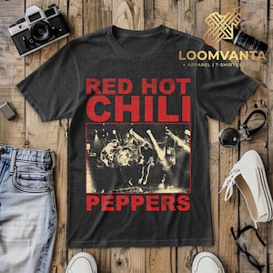 Könnte beinhalten: Ein anthrazitfarbenes Kurzarm-T-Shirt mit einem roten, verwaschenen Grafikdruck, der RED HOT CHILI PEPPERS über und unter einem schwarz-weißen Konzertfoto einer Band auf der Bühne mit hellen Bühnenlichteffekten zeigt.