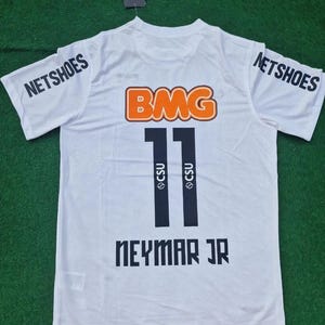 Peut inclure: Un maillot blanc à manches courtes avec l'inscription NETSHOES sur les deux manches, un grand logo orange BMG, le numéro 11 avec le texte CSU à l'intérieur, et le nom NEYMAR JR imprimé en noir au dos, avec une petite étiquette de marque.