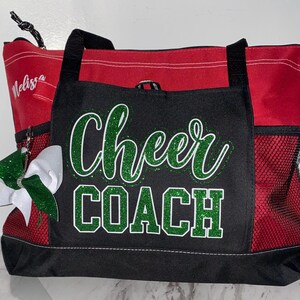 May include: Red and black tote bag with the words "Cheer COACH" in green glitter. The bag has black handles and a side pocket. A white and green bow is attached to the side. The name "Melissa" is written on the side.