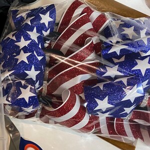 May include: A set of red, white, and blue glitter ribbon bows with a star pattern. The bows are packaged in a clear plastic bag.