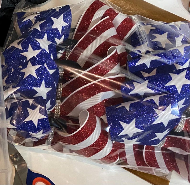 May include: A set of red, white, and blue glitter ribbon bows with a star pattern. The bows are packaged in a clear plastic bag.