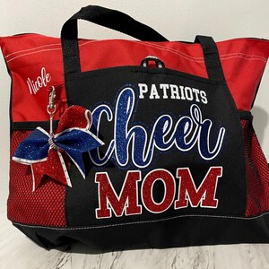 May include: Red and black tote bag with "Patriots Cheer Mom" text in blue and red glitter. Features a red and blue bow with a silver clip. Includes a side pocket and a black handle.