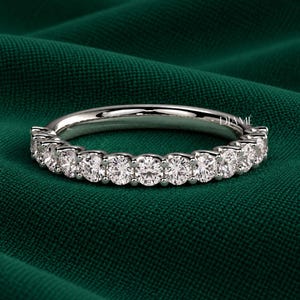 May include: A silver-toned band ring featuring a row of eleven round, clear, faceted stones set in a shared prong setting. The word DIAMÉ is printed in small white letters on the upper right side of the band, showcasing a polished metal finish.