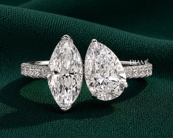 May include: A silver-toned ring featuring a large marquise-cut stone and a pear-cut stone set side-by-side. The band is encrusted with small pavé stones along the sides. The word DIAMÉ is printed in small white letters on the right side of the ring.