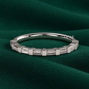 May include: A silver-toned ring featuring a series of clear, rectangular baguette-cut stones set in a row, separated by small metal bars. The band has a polished finish and the word DIAMÉ is printed in small white letters on the inner surface.
