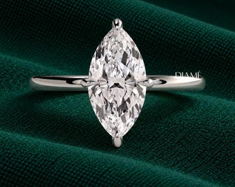 May include: A silver-toned ring featuring a large, faceted marquise-cut clear stone held by a six-prong setting on a smooth, polished band. The word DIAMÉ is printed in small white capital letters on the right side of the ring band.