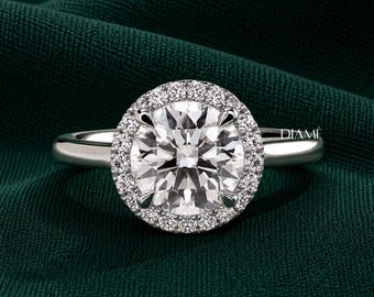 May include: A silver-toned ring featuring a large, round, faceted center stone surrounded by a halo of smaller, round, brilliant-cut stones. The band is smooth and polished. The word DIAMÉ is printed in small white letters on the right side.