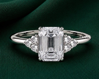 May include: A silver-toned ring featuring a large emerald-cut center stone flanked by three smaller round-cut stones on each side. The band is smooth and polished, and the word DIAME is printed in small white letters on the right side of the band.