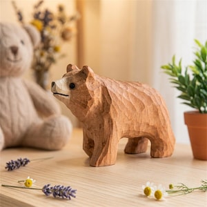 Op de afbeelding: Een handgesneden houten berenbeeldje met een lichtbruine afwerking en zichtbare beitelsporen. De beer staat in een staande positie en heeft een lichtere snuit, een kleine zwarte neus en donkere ogen, wat zorgt voor een getextureerd oppervlak.
