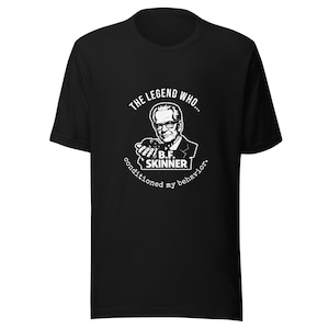 Può includere: Una t-shirt nera a maniche corte con una stampa grafica bianca di B.F. Skinner che tiene in mano un ratto. Il testo recita THE LEGEND WHO... B.F. SKINNER conditioned my behavior. Il disegno è centrato sul petto della maglietta.