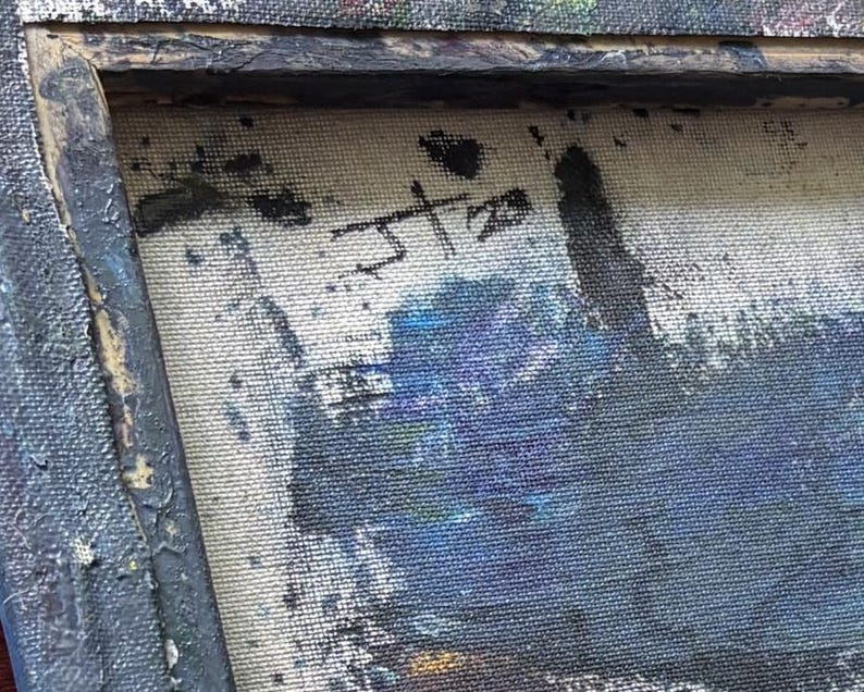 May include: A close-up of a textured canvas painting featuring a dark, weathered wooden frame. The artwork displays a signature with the letters JT and the number 20 in black paint. The composition includes deep blue, black, and white pigments.