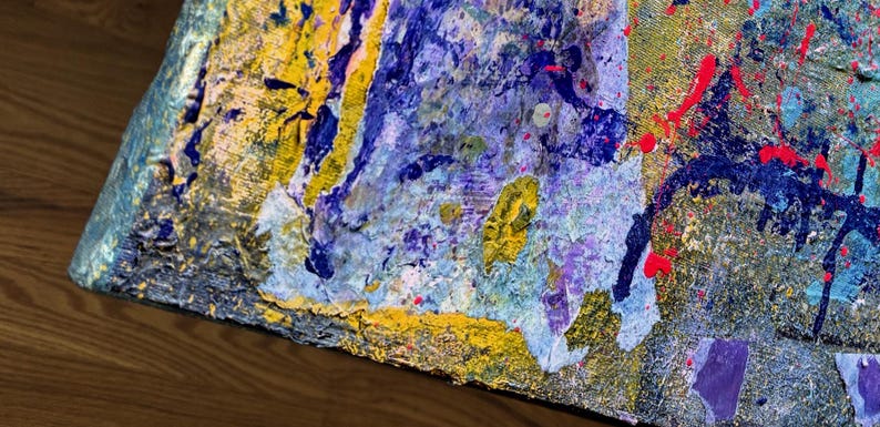 May include: An abstract painting on canvas featuring a thick, textured application of paint in shades of deep blue, bright yellow, light purple, and metallic gold, accented with vibrant red splatters across the surface of the artwork.