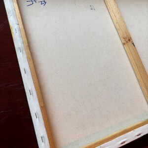 Pu&ograve; includere: Il retro di una tela rettangolare tesa su un telaio in legno chiaro. La tela &egrave; fissata con punti metallici lungo i bordi. Un segno blu scritto a mano che riporta H '23 &egrave; visibile nell'angolo in alto a sinistra del tessuto della tela.