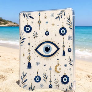 Pode incluir: Uma capa transparente para tablet com um padrão impresso de amuletos de olho grego azul, luas crescentes douradas e ramos de folhas azul-escuras. O design inclui um grande motivo de olho central rodeado por vários pingentes, estrelas e flores.