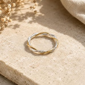 Peut inclure: Une bague fine au design torsadé composée de deux anneaux entrelacés, l'un dans un ton argenté poli et l'autre dans un ton doré poli, formant une forme circulaire continue avec une finition métallique lisse et réfléchissante sur l'ensemble.