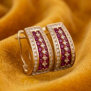 Puede incluir: Un par de pendientes de aro de oro con un diseño rectangular curvado. El centro de cada pendiente está engastado con múltiples rubíes rojos redondos y pequeños diamantes blancos, enmarcados por un borde de diminutos diamantes en pavé.