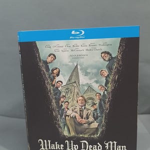 Puede incluir: Una caja de Blu-ray para la película Wake Up Dead Man: A Knives Out Mystery. La portada presenta una iglesia de piedra central rodeada por un elenco de personajes enmarcados dentro de una zanja de tierra oscura en forma de V sobre un cielo claro.