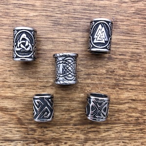 May include: Five silver metal hair beads with different Celtic knot designs. The beads are round and have a smooth surface.