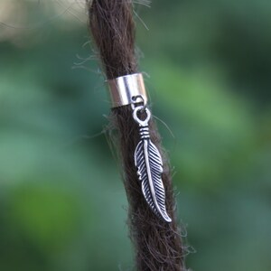 Op de afbeelding: Zilveren dreadlock-kraal met een veerbedel. De kraal is een eenvoudige cilinder en de veerbedel is gedetailleerd en realistisch.