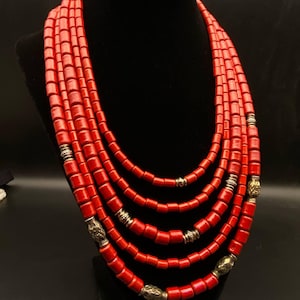 May include: A multi-strand necklace featuring five layers of cylindrical red beads. The strands are interspersed with metallic silver-toned spacers and decorative beads that have intricate embossed patterns, creating a layered appearance.