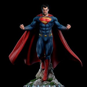 May include: A detailed collectible statue of Superman featuring a muscular figure in a textured blue suit with a red cape, a yellow and red chest emblem, and red boots. The figure stands on a rocky base with green moss accents against a black background.