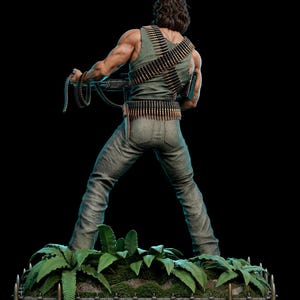 May include: A muscular figure with long brown hair, wearing a green tank top and pants, stands on a base with green ferns. The figure is adorned with two crossed bandoliers of ammunition and holds a machine gun with a hanging belt of bullets.