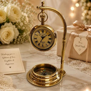 May include: A polished brass desk clock and compass set featuring a circular clock face with Roman numerals, the text Victoria London 1915, and a crown icon. The clock hangs from a curved brass stand above a circular magnetic compass base.
