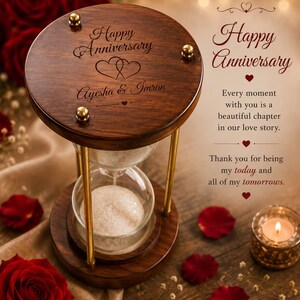 May include: A wooden hourglass with gold-toned metal supports and a glass sand timer. The top wooden lid is engraved with "Happy Anniversary," two hearts, and the names "Ayesha & Imran." The text "Happy Anniversary" and a romantic quote are visible.