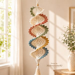 May include: A vertical hanging decoration featuring five spiraling crochet segments in cream, green, terracotta, yellow, and blue. The piece is accented with two wooden beads and a bottom tassel. The text Design by Moderncrochet4U is visible.