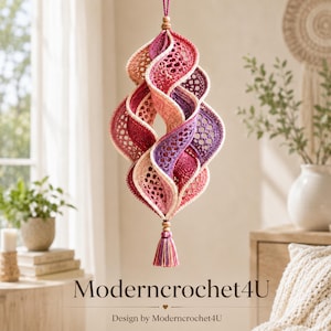 May include: A hanging crochet ornament featuring a spiraling, multi-layered design in shades of pink, purple, and cream. The piece is constructed with intricate openwork patterns, finished with a wooden bead at the top and a matching tassel at the bottom.