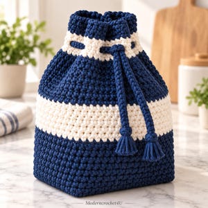 May include: A navy blue and cream white crochet drawstring bag featuring a textured stitch pattern, a wide horizontal cream stripe, and a matching navy blue braided cord closure with two small tassels at the ends. The text Moderncrochet4U is visible.