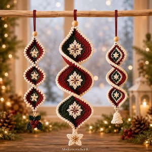 Könnte beinhalten: Drei hängende Häkelornamente in Dunkelgrün, Dunkelrot und Creme. Jedes zeigt ein Rautenmuster mit weißen Schneeflockenmotiven, Holzperlen und roten Kordelaufhängern. Links mit Stechpalmenblättern, in der Mitte ein Stern und rechts eine kleine Glocke.